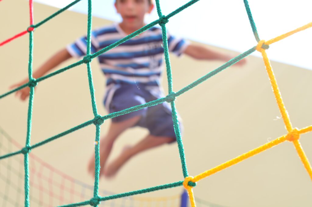 Child jumping on a trampoline behind some colorful netting