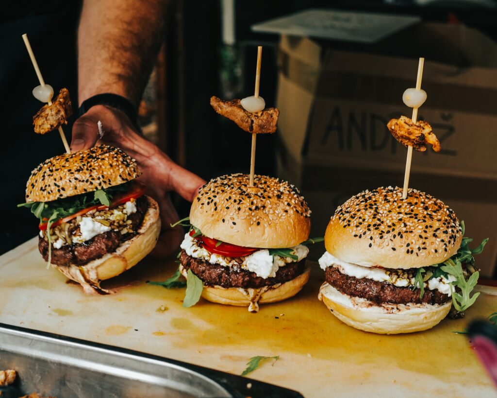 Three burgers with sesame seed buns on a wooden cutting board