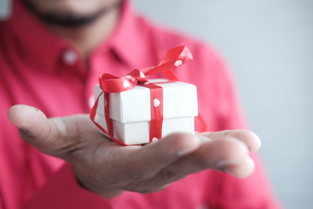 Person holding a small white box tied up with red ribbon and a bow.