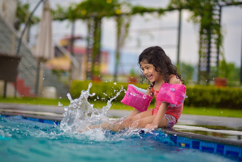 Girl with pink floaties splashing her feet in the pool.